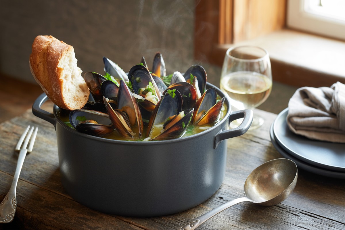 Moules au vin blanc servies dans cocotte noire, persil frais et pain rustique